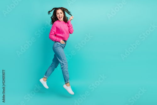 Full size photo of cute girl with wavy hairdo pink pullover jeans sneakers hand in pocket touch hair isolated on teal color background