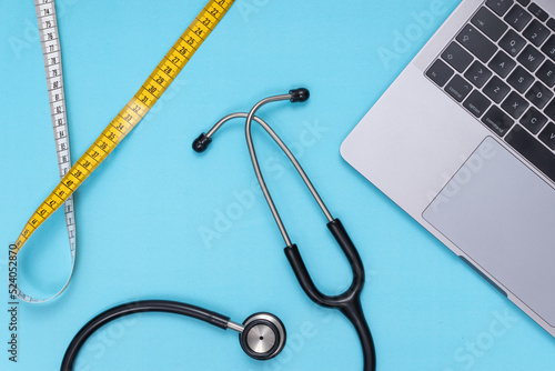 black stethoscope, laptop, tape measure, blue isolated background