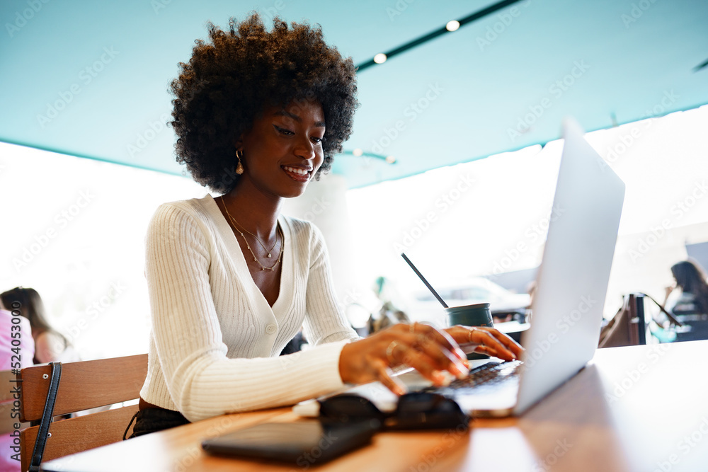 Leinwandbild Motiv - fotofabrika : Smiling young african woman sitting with laptop in cafe