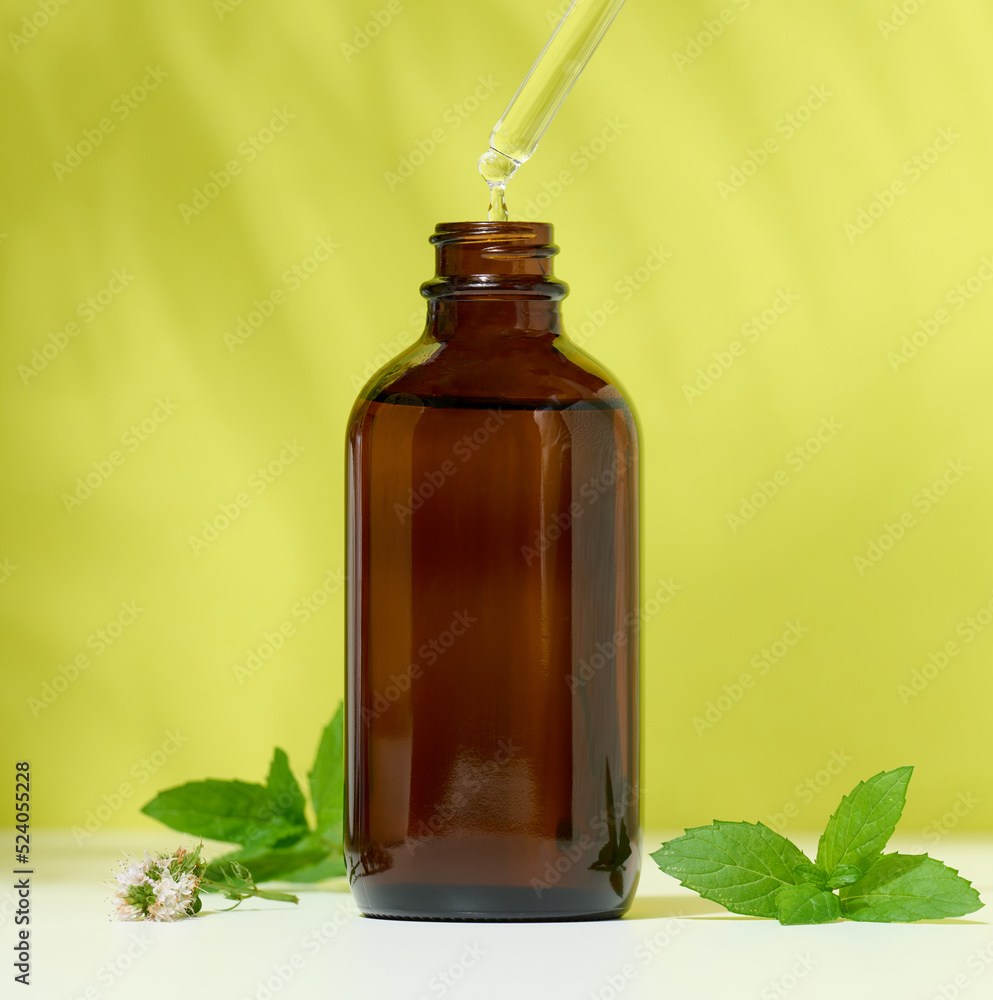 Brown glass bottle with a cosmetic product and a pipette with a drop, green background. Brown glass bottle with a cosmetic product and a pipette with a drop, green background.