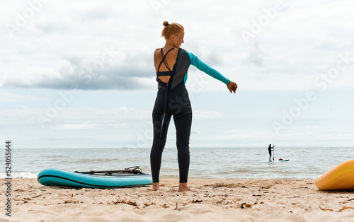 A woman puts on a wetsuit on the beach and is going for a walk on the sea on a SUP board. Active recreation.