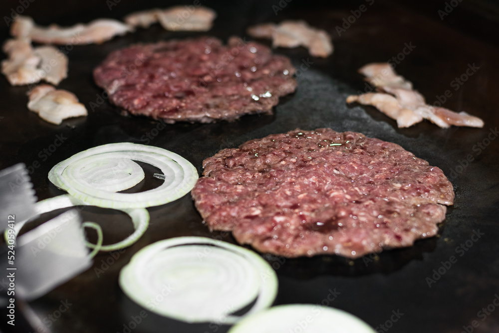 close-up detail shot of two ground hamburger meats with onion and tosino around, cooking in a colombian street food grill or fast food stand, beef on the grill. food concept close-up detail shot of two ground hamburger meats with onion and tosino around, cooking in a colombian street food grill or fast food stand, beef on the grill. food concept
