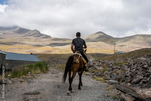 a rider on a brown horse gallops against the backdrop of mountains and an alpine lake in Armenia