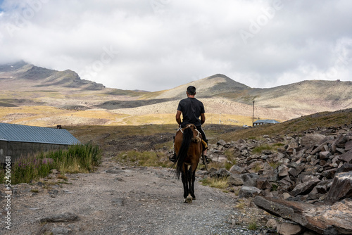 a rider on a brown horse gallops against the backdrop of mountains and an alpine lake in Armenia
