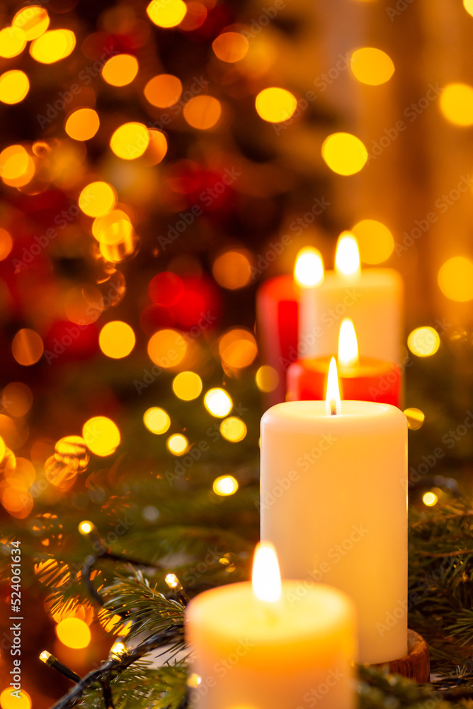 Cozy, magical atmosphere, Christmas tree on the background. Burning candles surrounded by bright garland lights, vertical shot, copy space