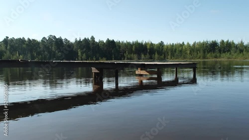 Natural landscape. A clear sunny day. A forest lake on which there is a wooden bridge. Clear water with small waves, in which the sky is reflected.