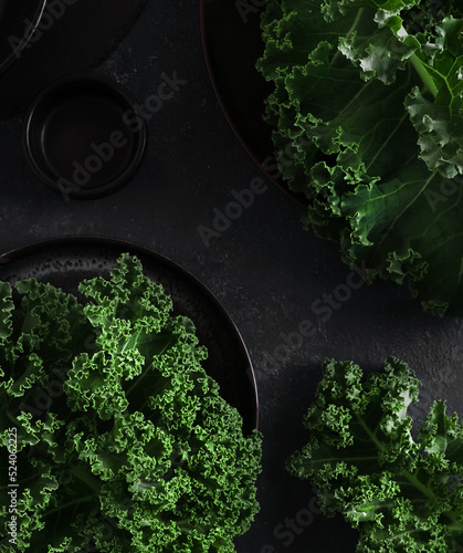 Fototapeta Naklejka Na Ścianę i Meble -  Green kale cabbage leaves on dark backgtound. Textured leaves in  black plate. Top view closeup. Healthy food concept.