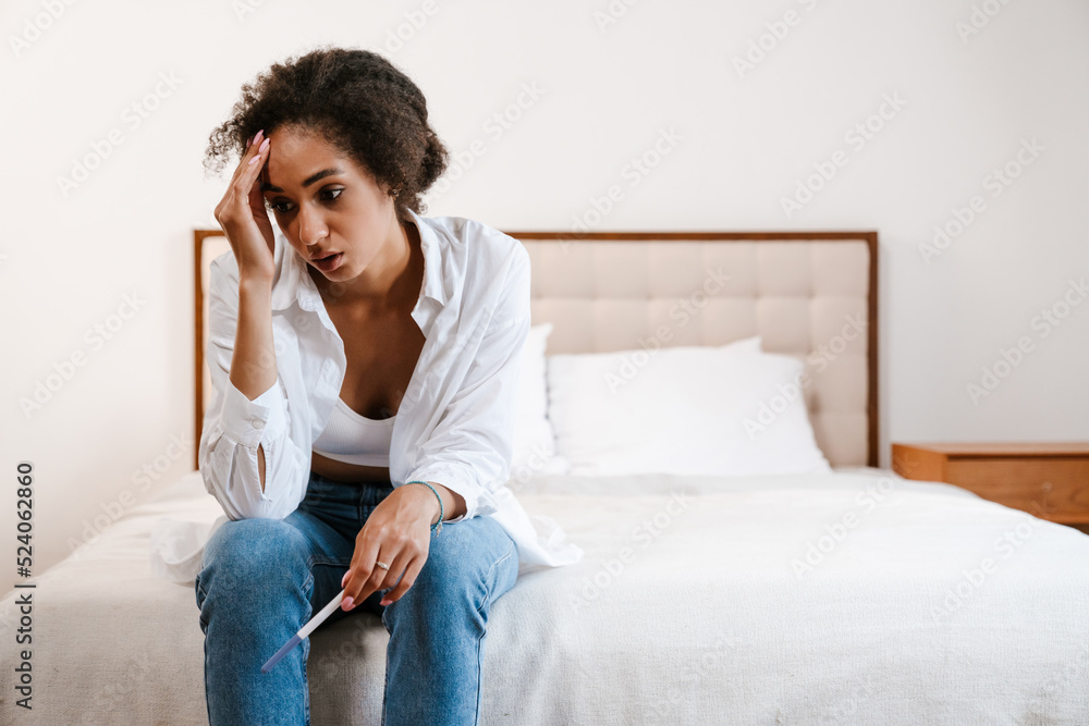 Young black woman being upset while holding pregnancy test at home Young black woman being upset while holding pregnancy test at home