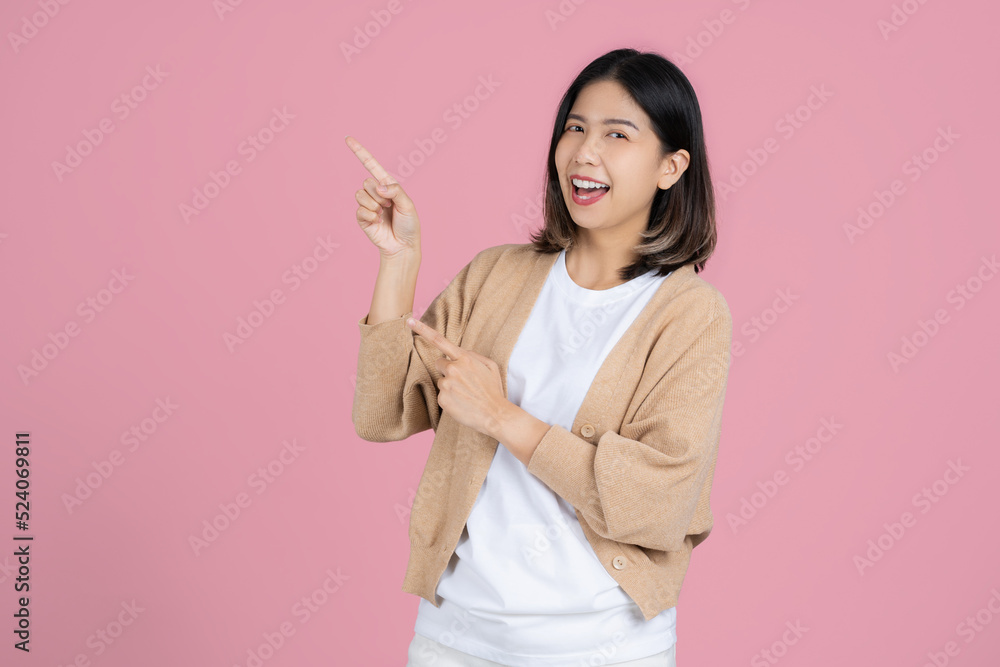 Smiling young asian woman standing pointing index fingers aside up on mock up copy space isolated on pink background studio portrait Smiling young asian woman standing pointing index fingers aside up on mock up copy space isolated on pink background studio portrait