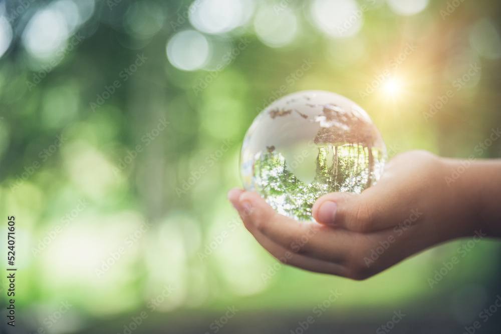 Human hands holding earth sphere crystal or sustainable globe glass with sunlight at green nature background in ecology environment forest. concept of conservation environmental, protection planet. Human hands holding earth sphere crystal or sustainable globe glass with sunlight at green nature background in ecology environment forest. concept of conservation environmental, protection planet.