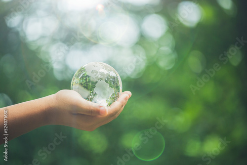 Human hands holding earth sphere crystal or sustainable globe glass with sunlight at green nature background in ecology environment forest. concept of conservation environmental, protection planet.