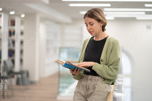 Reading is my passion. Focused middle-aged woman literature fan holding open book in hands, selective focus. Mature female visiting library gaining knowledge from books, bookworm person