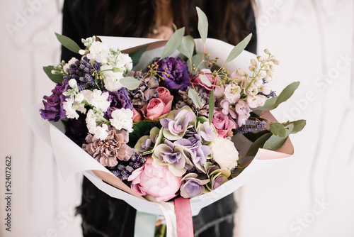 Very nice young woman holding big and beautiful bouquet of fresh peonies, roses, carnations, hydrangea, lupines, matthiolas, eucalyptus, eustoma in white purple colors, cropped photo, bouquet close up