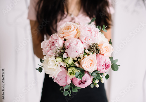 Very nice young woman holding big and beautiful wedding bouquet of fresh peony, roses, eustoma, brunia, eucalyptus in pastel cream and pink colors, cropped photo, bouquet close up