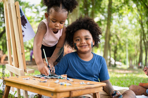 Portrait African American kid boy and girl painting in the park	