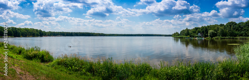 Panoramic view of the lake on a sunny day. Floating sailboats and a forest in the background. Paprocany Lake, Tychy, Poland.