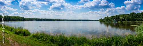 Fototapeta Naklejka Na Ścianę i Meble -  Panoramic view of the lake on a sunny day. Floating sailboats and a forest in the background. Paprocany Lake, Tychy, Poland.