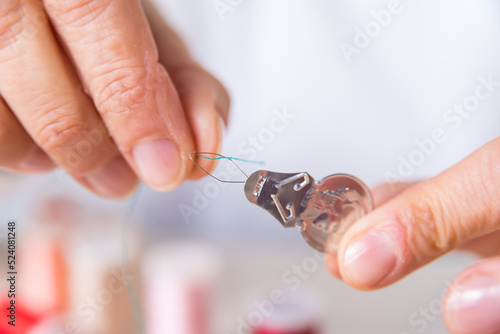 hands threading a needle, colored threads, dressmaker, atelier, seamstress, sewing clothes, embroidering a fabric, needle and thread, selective focus