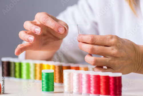 thread passing through the needle  many colors  dressmaker  atelier  sewing  sewing clothes  embroidering a fabric  selective focus