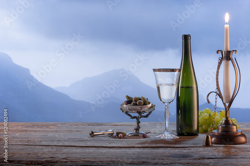 Natural view. Bottle of white wine with olives appetizers standing on wooden table isolated over foggy mountain background