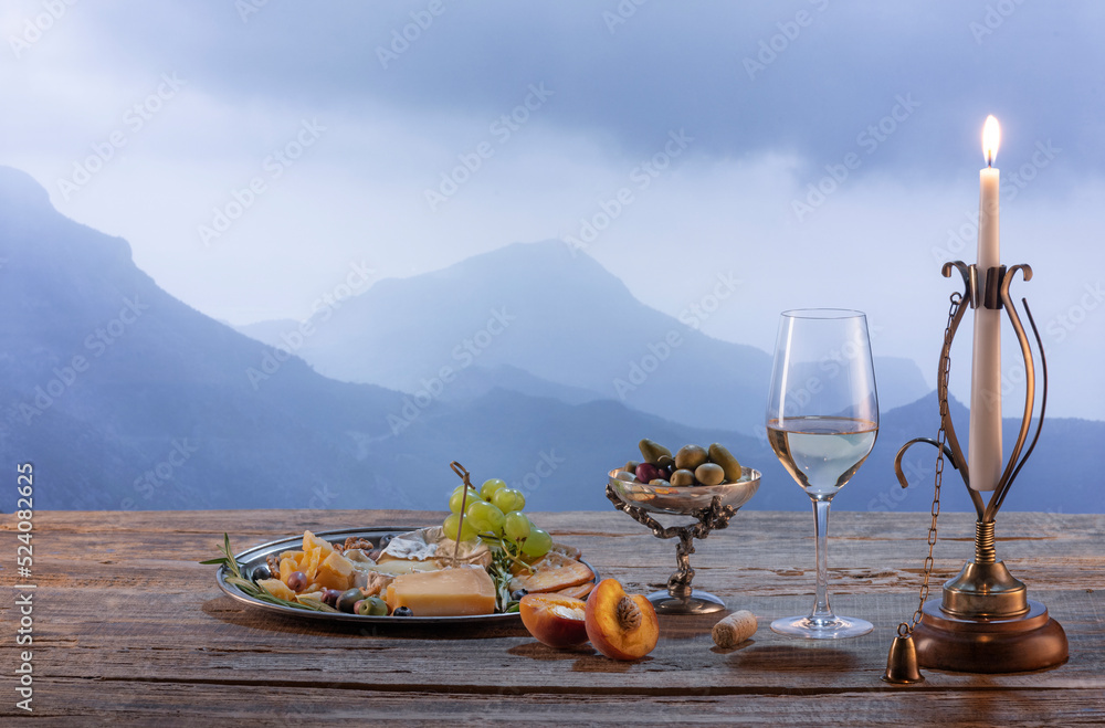 Fototapeta premium Vintage image of wine bottle, glass filled with delicious white wine isolated over beautiful nature landscape of mountains. Winemaking on countryside
