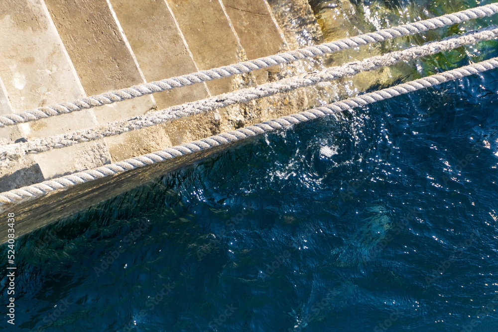 Top view of a staircase leading into the water with stretched white ropes and a bright ocean