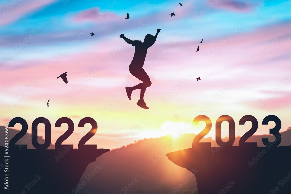 Silhouette man jumping between cliff with number 2022 to 2023 and birds flying at top of mountain. Freedom challenge and travel adventure holiday concept. Silhouette man jumping between cliff with number 2022 to 2023 and birds flying at top of mountain. Freedom challenge and travel adventure holiday concept.