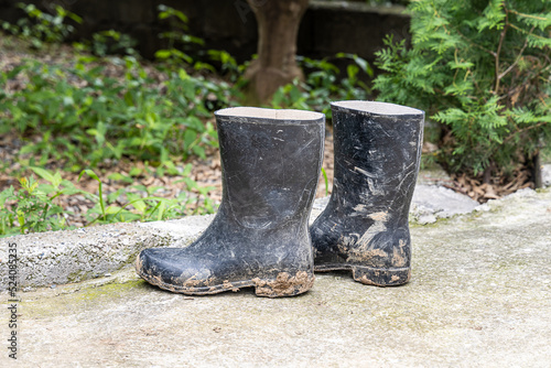 A pair of dirty black rubber boots is on a path in the garden after using