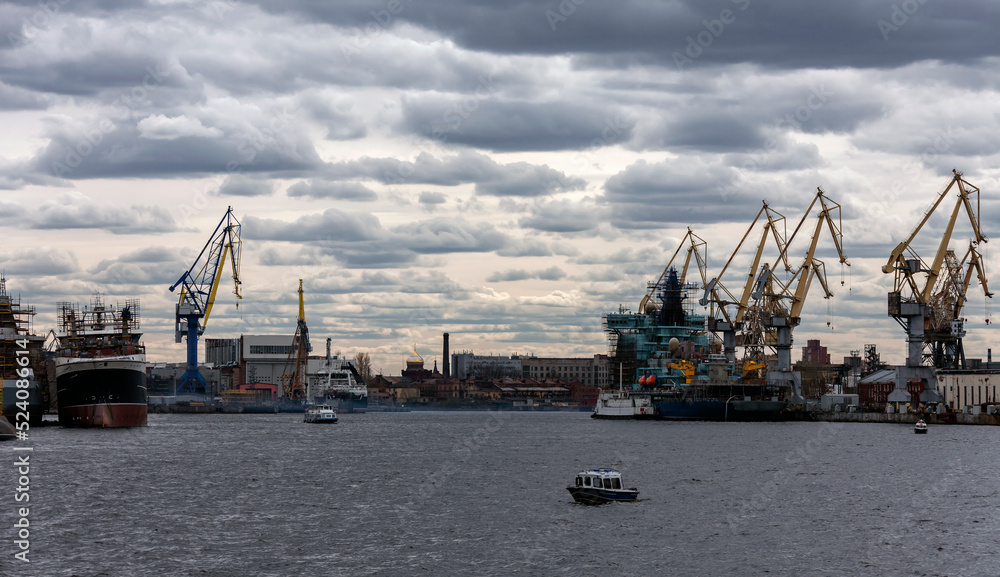 Water landscape in the lower reaches of the Neva River with cranes and ships at the mooring wall.