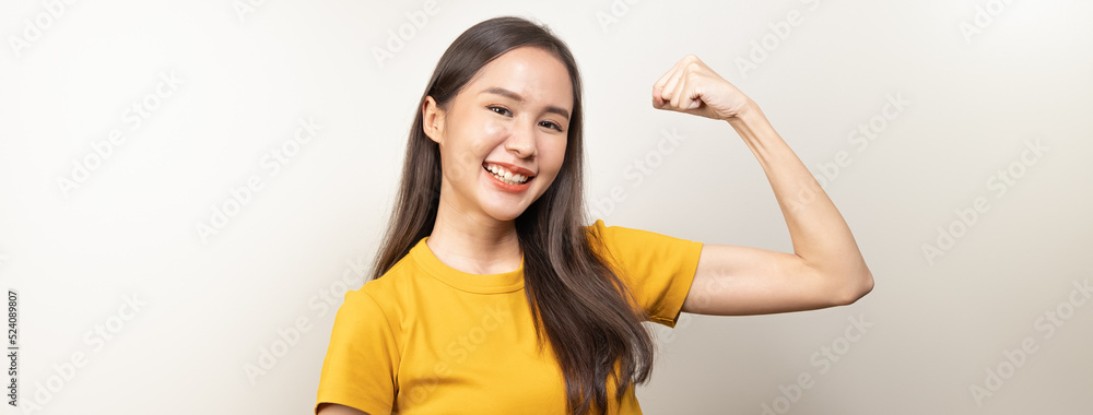 Asian young woman in yellow t shirt doing strong gesture isolated on background. Asian young woman in yellow t shirt doing strong gesture isolated on background.