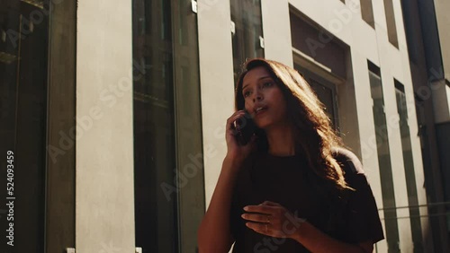 Young woman walking on sunny street talking by mobile phone with smile