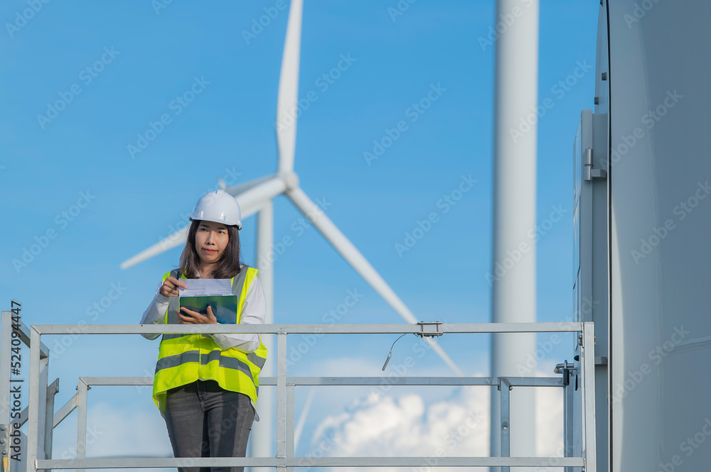 women engineer working and holding the report at wind turbine farm Power Generator Station on mountain,Thailand people women engineer working and holding the report at wind turbine farm Power Generator Station on mountain,Thailand people