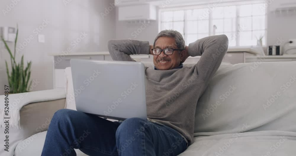 Happy, smiling elderly man enjoying entertainment on laptop while relaxing on sofa at home. Mature and retired male loving his fast internet, good wifi and high speed connection, streaming service.