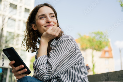 Young woman looking positively to the side with cell phone in hand