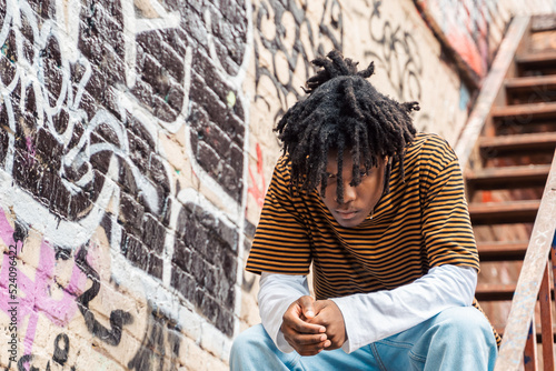 Young handsome stylish black man with natural hair dreadlocks. Afroamerican guy.Stairs,wall painted with graffiti in poor quarter of street art culture city district.African american skateboarder man photo