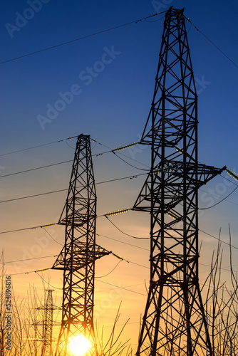 Electricity poles and electric power transmission lines against at sunset on a winter day with flickering air. High Voltage towers provide power supply over a long distance.