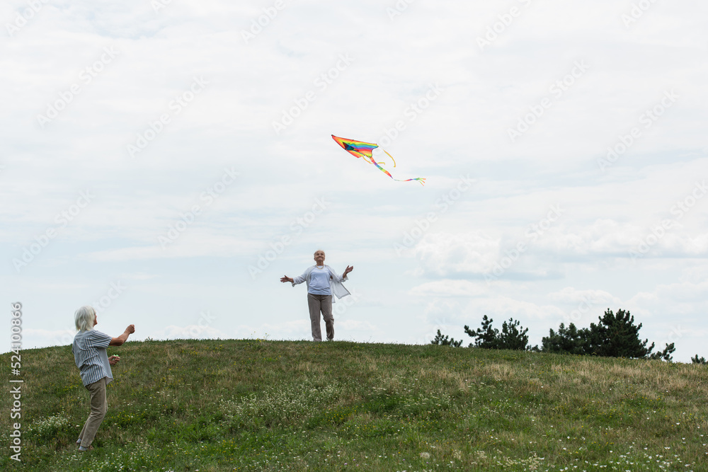 cheerful senior woman in casual clothes looking at kite near husband on green hill. cheerful senior woman in casual clothes looking at kite near husband on green hill.