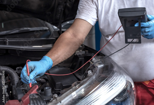 mechanic using car battery meter checking batter problem in auto repair service, vehicle maintenance and repair concept