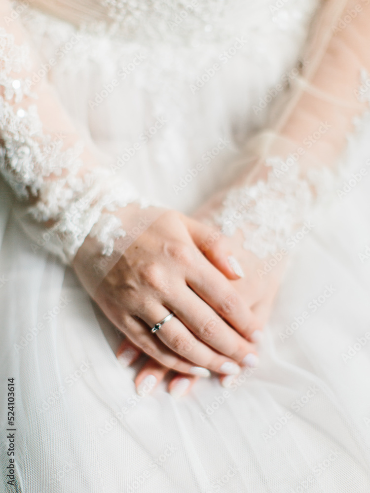 Hands of the bride with a wedding manicure and in a wedding ring close-up against the background of a wedding dress. Hands of the bride with a wedding manicure and in a wedding ring close-up against the background of a wedding dress.