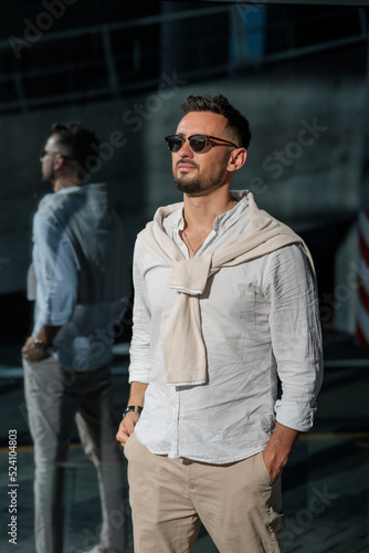 Wallpaper Mural Brutal bearded man hipster in fashionable summer white clothes in sunglasses in stylish white sneakers stands on a sunny day near a glass building. Nice guy. Trendy menswear. Street style Torontodigital.ca