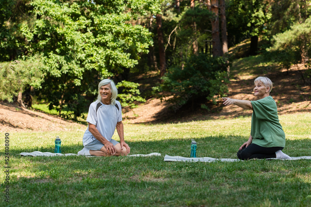 full length of senior woman pointing with finger near happy husband on fitness mat in green park. full length of senior woman pointing with finger near happy husband on fitness mat in green park.