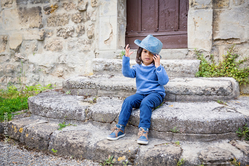 Little handsome baby boy sitting on ancient stone stairs and playing outdoor with straw hat in old city © svittlana