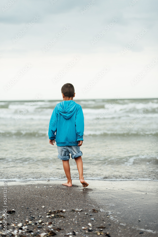 Sad alone kid standing on beach, looking at sea and thinking. The end of summer. sadness about end of vacation
