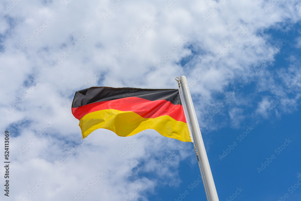 German flag waving in the wind. It is a beautiful sunny summer day, with blue sky and white clouds in the background. German flag waving in the wind. It is a beautiful sunny summer day, with blue sky and white clouds in the background.