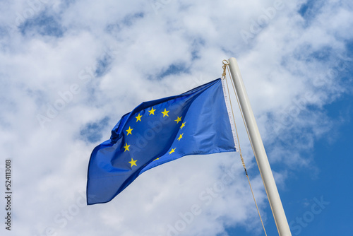 European Union flag waving in the wind. It is a beautiful sunny summer day, with blue sky and white clouds in the background.