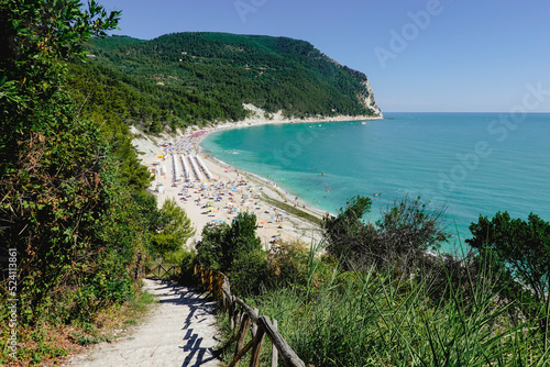 Blue sea in sunny day close to the forest in the Conero natural park - Italy. During touristic season is full of umbrella and people. photo