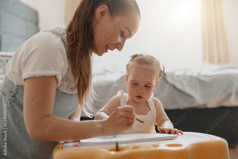 Little smiling girl painting with her mother at home while spending time together Little smiling girl painting with her mother at home while spending time together