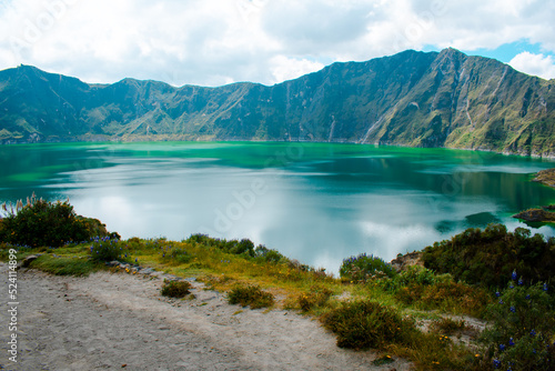 Quilotoa lagoon inside a volcano's crater in Latacunga, Ecuador. Hike and touristic destination. Turquoise water reflecting cloudy sky.