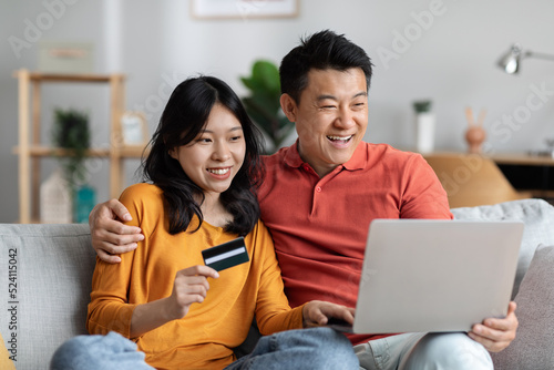 Smiling asian man and woman using computer and credit card