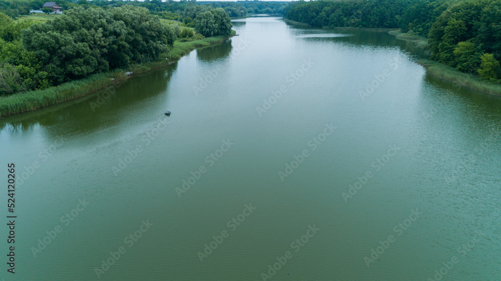 Aerial view fisherman is fishing sitting on an inflatable boat in lake. Drone wide shot adult man sailing on a boat to fish